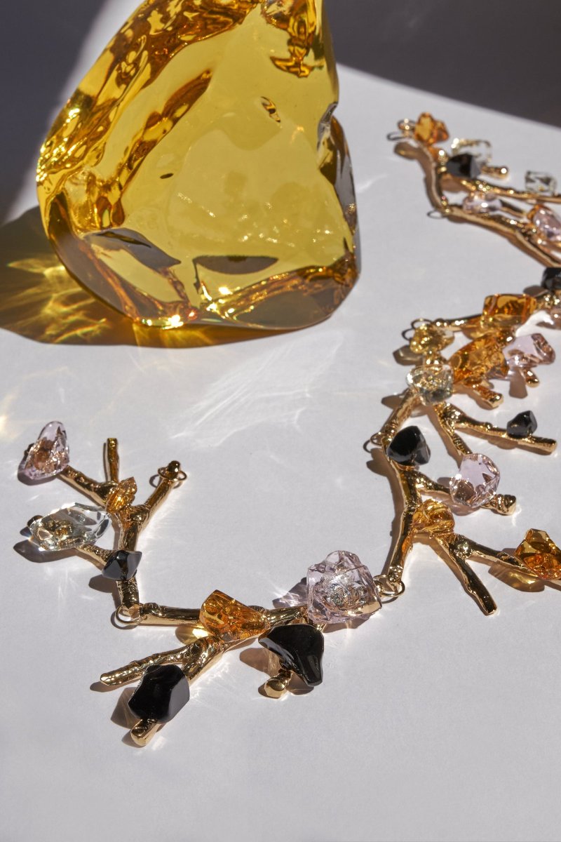 An amber crystal block beside a gold-coloured chain, its branching metal holding clear, pink and black splinters
