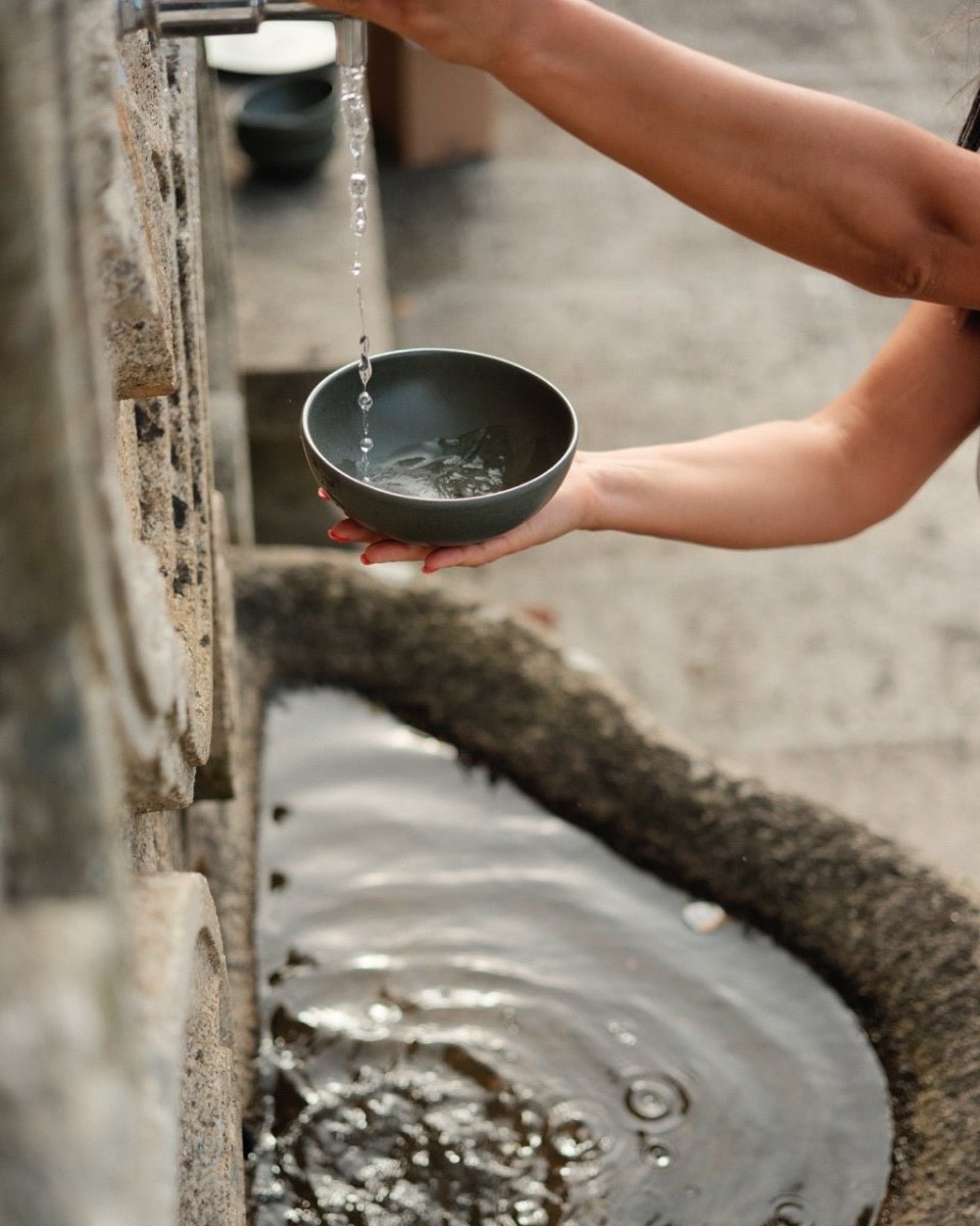 A bowl held under the spout of an old stone fountain.