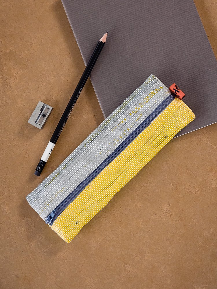 A woven pencil case in yellow and grey, beside a pencil and a sharpener.