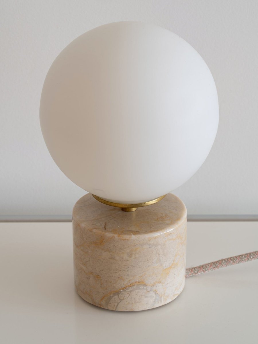 The Pauline lamp unlit, a white opaline globe on a slim brass collar above a short cylinder of veined Lioz stone.