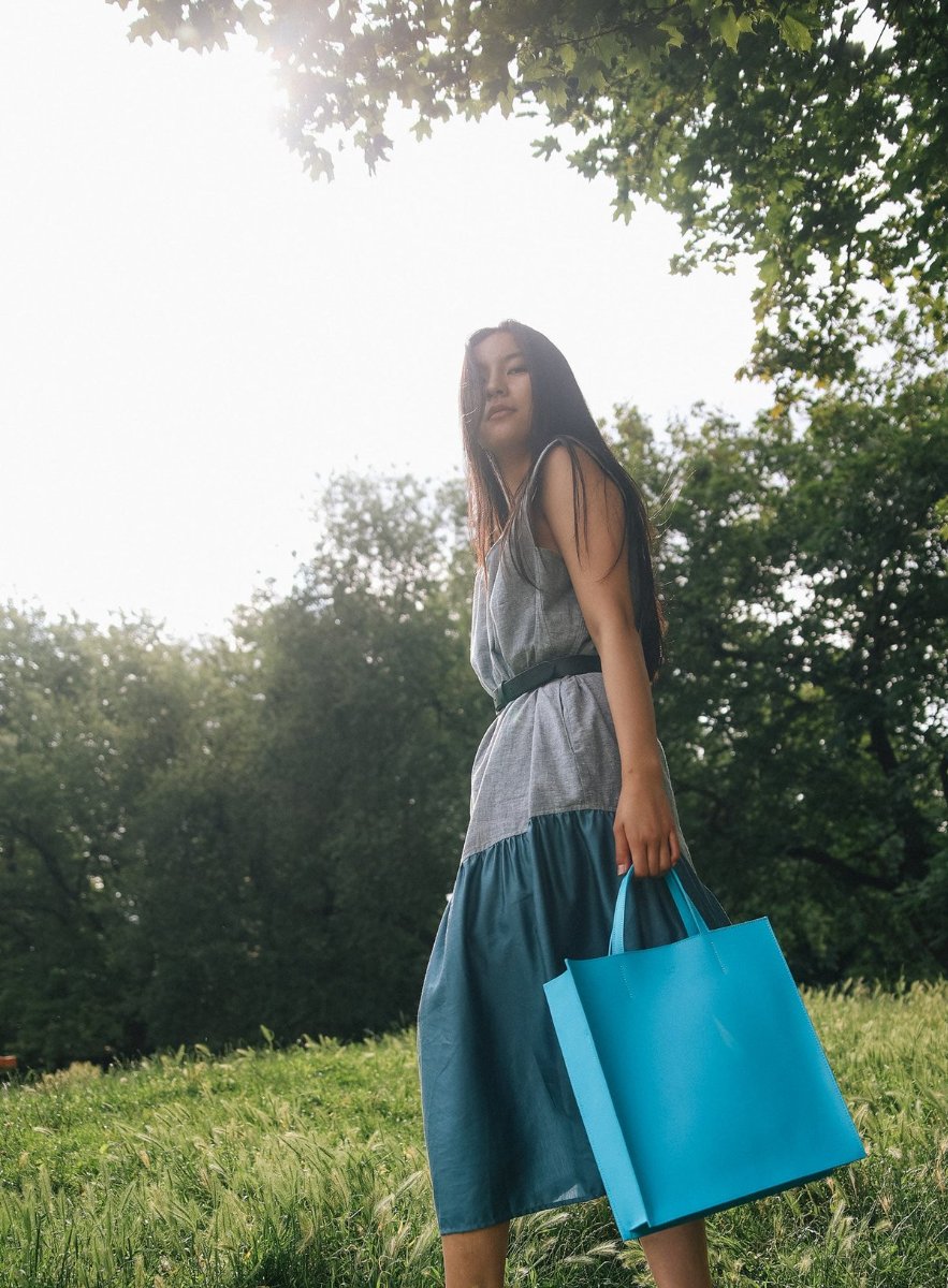 A turquoise leather tote held at her side in a sunlit meadow.