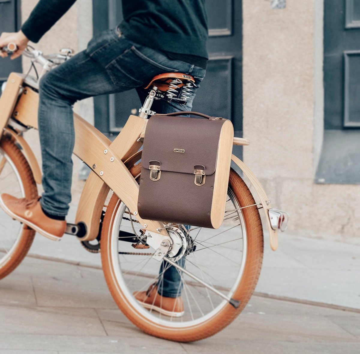 A wooden bicycle in traffic, a bag strapped behind the saddle