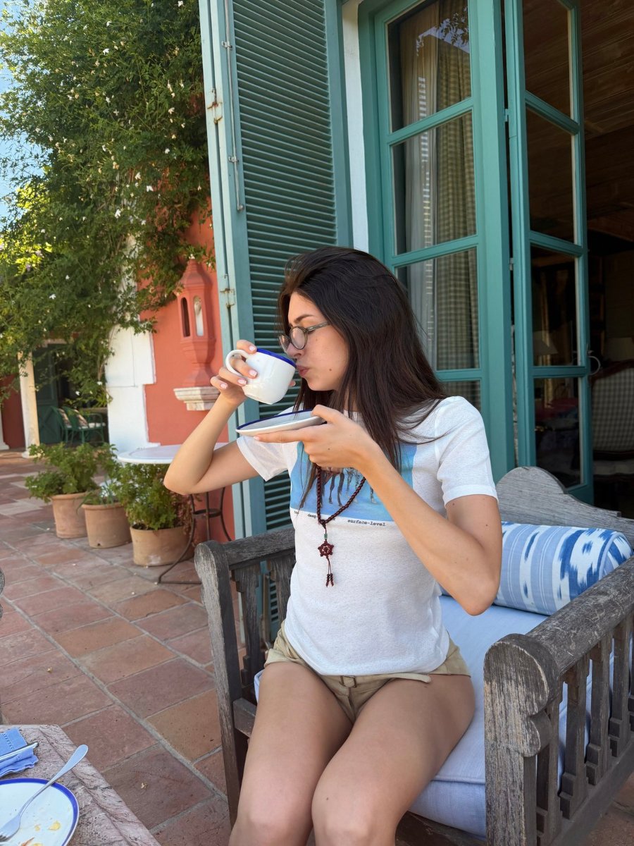 Drinking from a cup on a tiled terrace, the green shutters open behind.