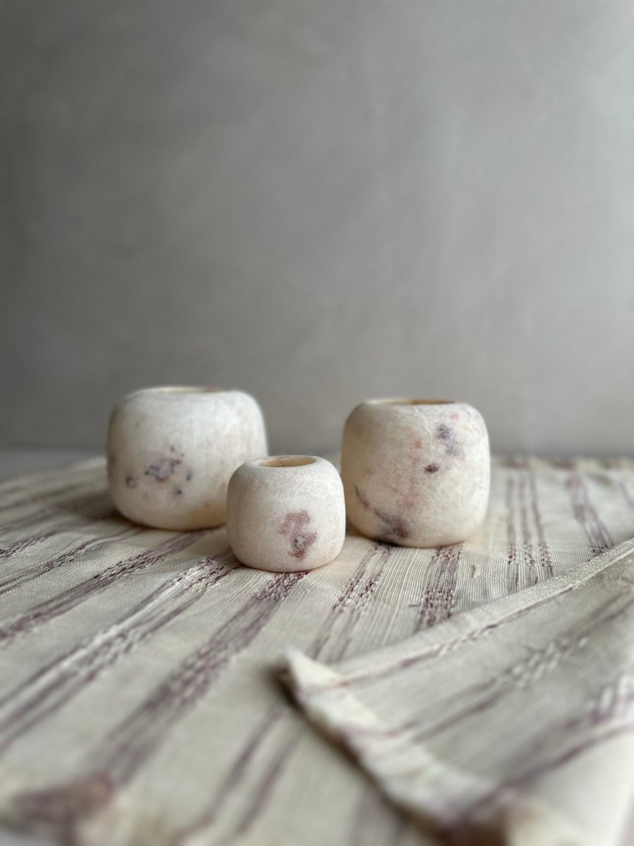 A handwoven cotton tea towel, three pale alabaster holders standing on it
