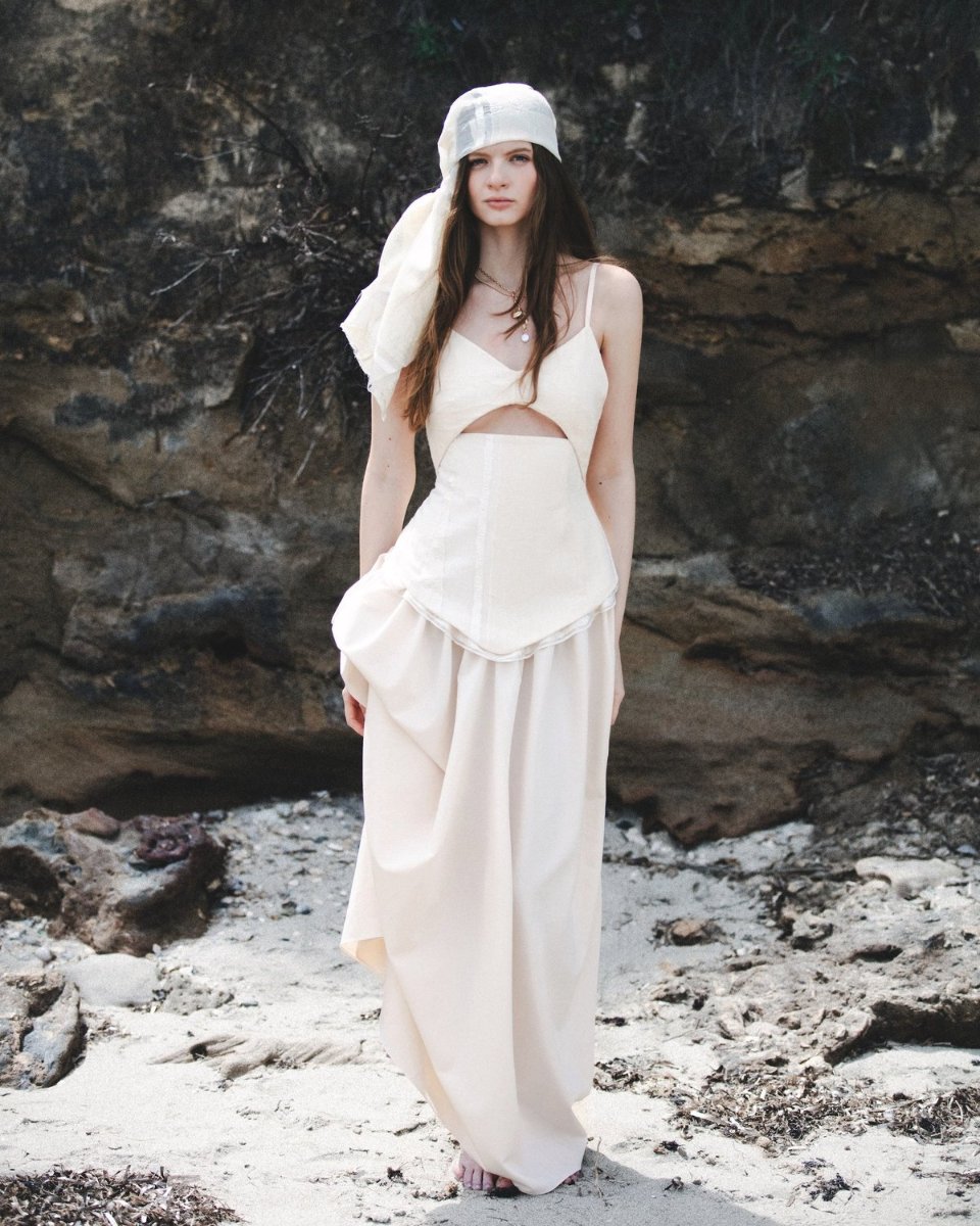 A full length pale dress from the debut collection, worn against dark rock