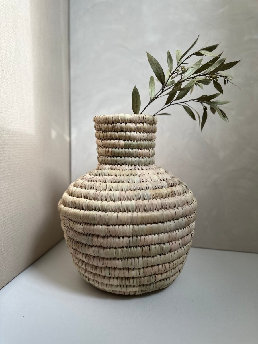 A woven palm leaf vase, a dried branch in its neck
