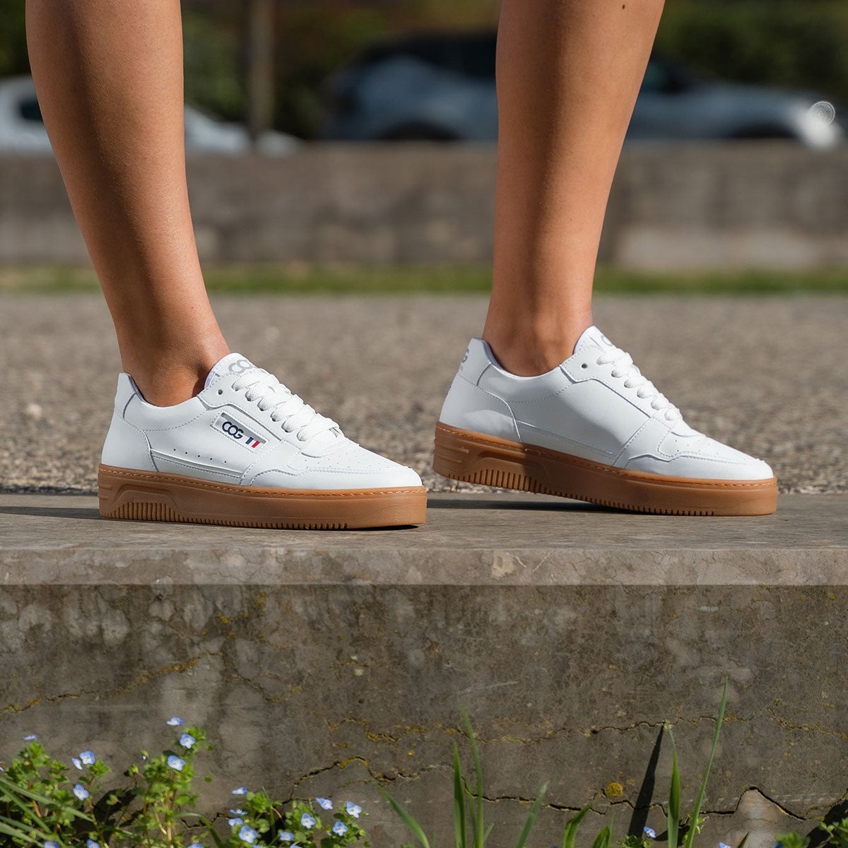 White low trainers with a gum sole, worn on a kerb.