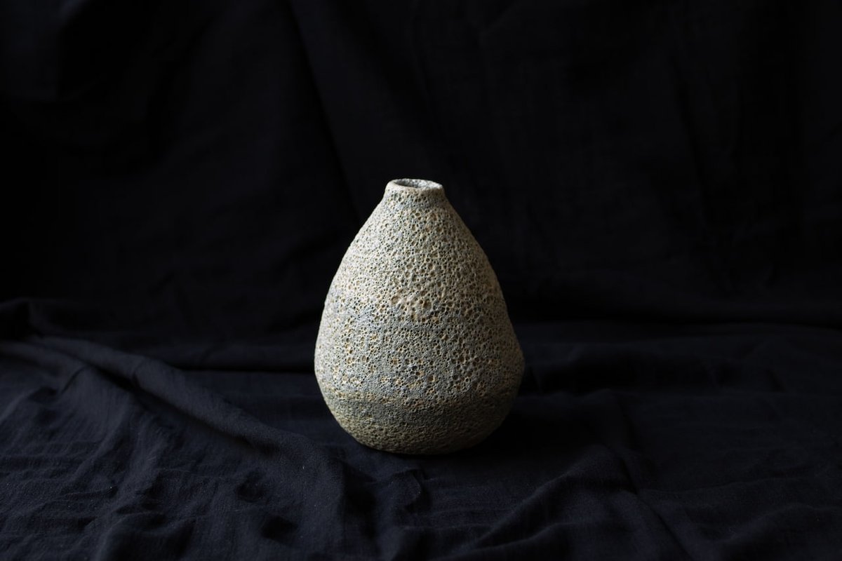 A lava-glazed vase, its surface cratered like a lunar plain.