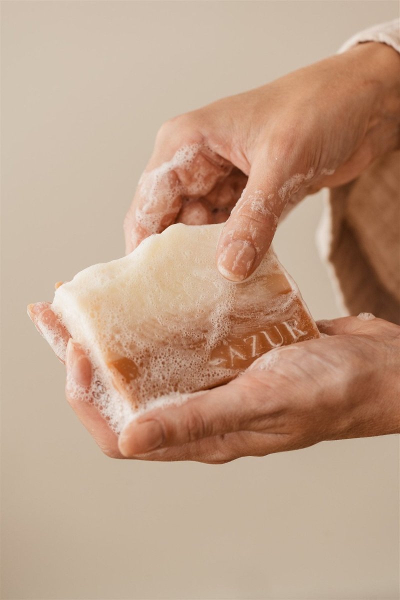 Two wet hands working a cream and peach marbled bar into thick lather.