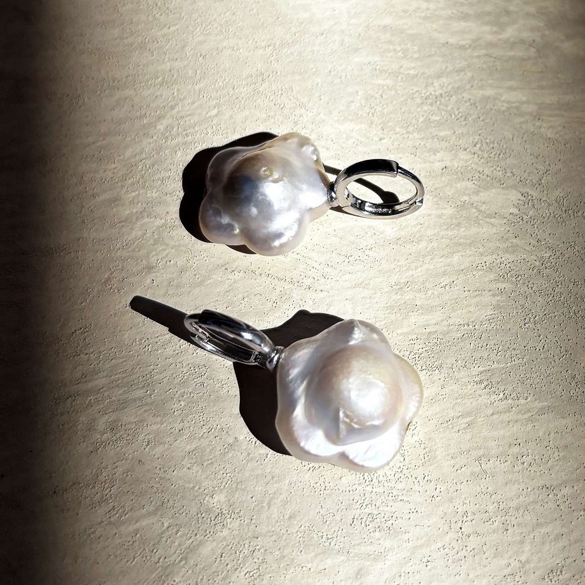 A pair of hoops, each holding a flower-shaped pearl.