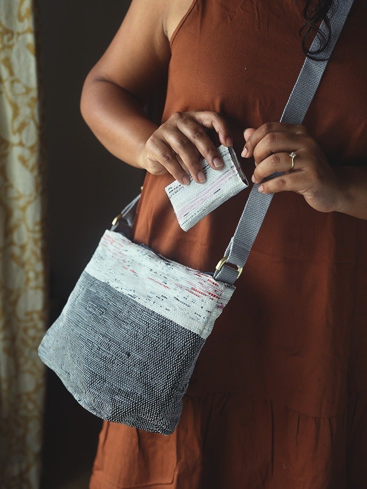 Hands lifting a small woven card case from a grey crossbody bag.