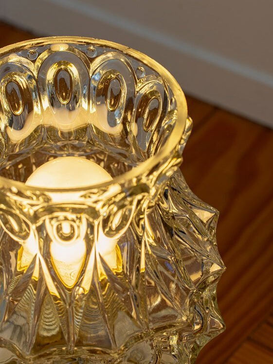 A close crop of a lit antique moulded glass shade, honey coloured light coming through the raised pattern, the bulb a soft shape inside.