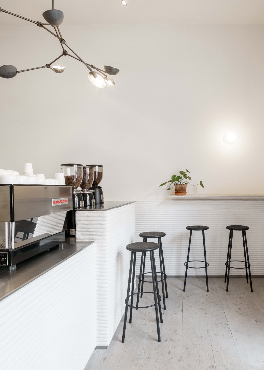 Weiß verputzte Theke, Espressomaschine, drei Hocker und eine Pflanze auf der Ablage.