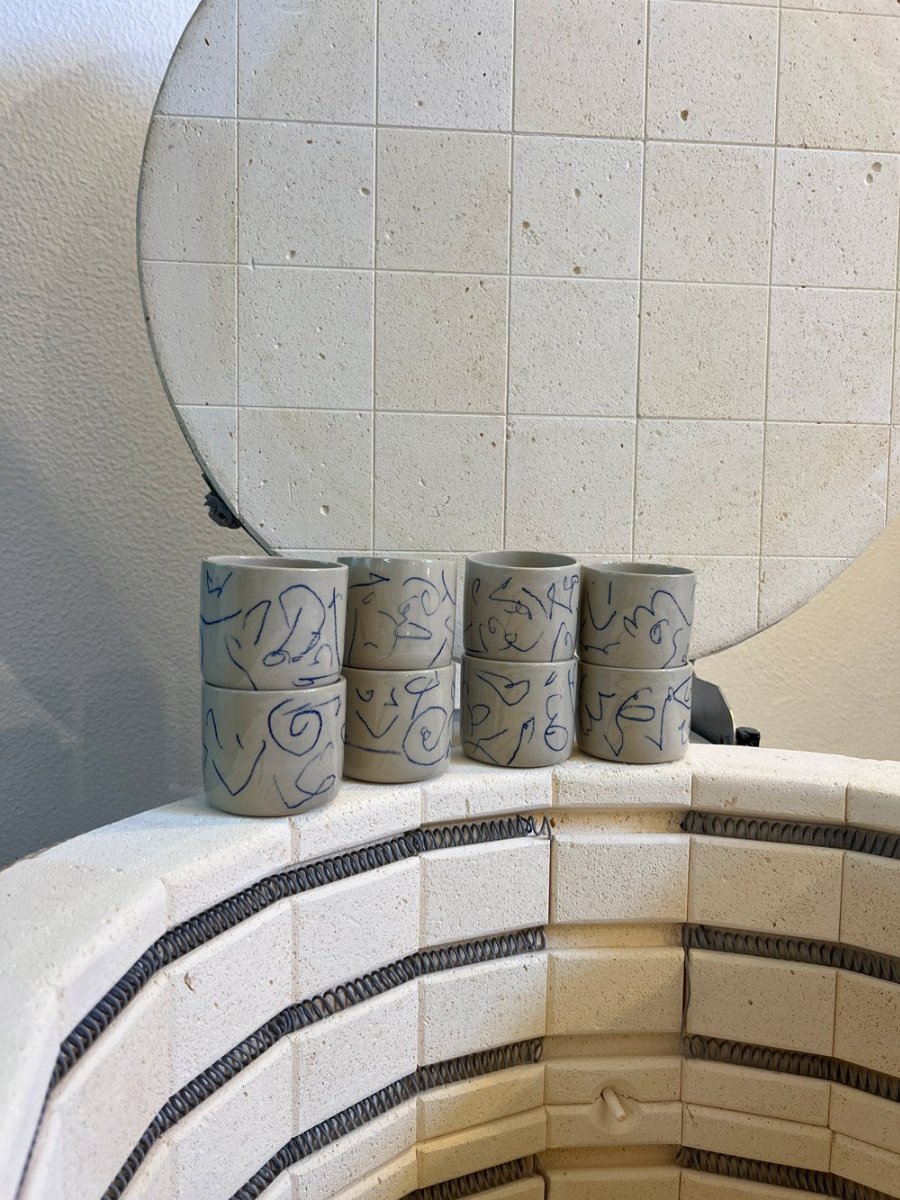 Cups with drawn lines, standing on the rim of the open kiln.
