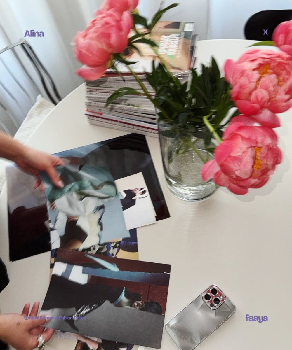 A hand moves cut photographic pieces around a white table, a glass of peonies beside them, a collage taking shape.