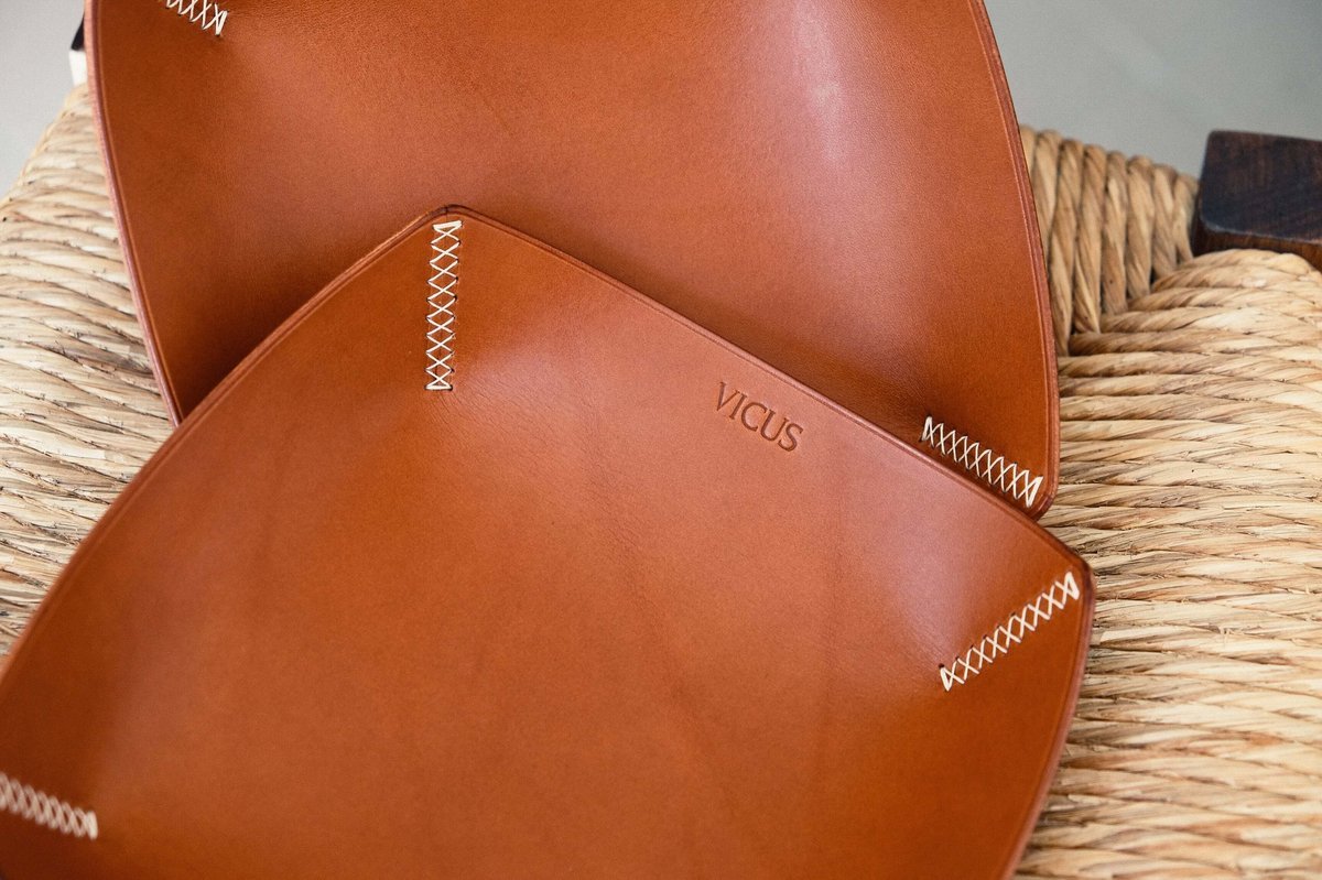 Two tan leather trays, each corner pulled together with hand cross stitching.