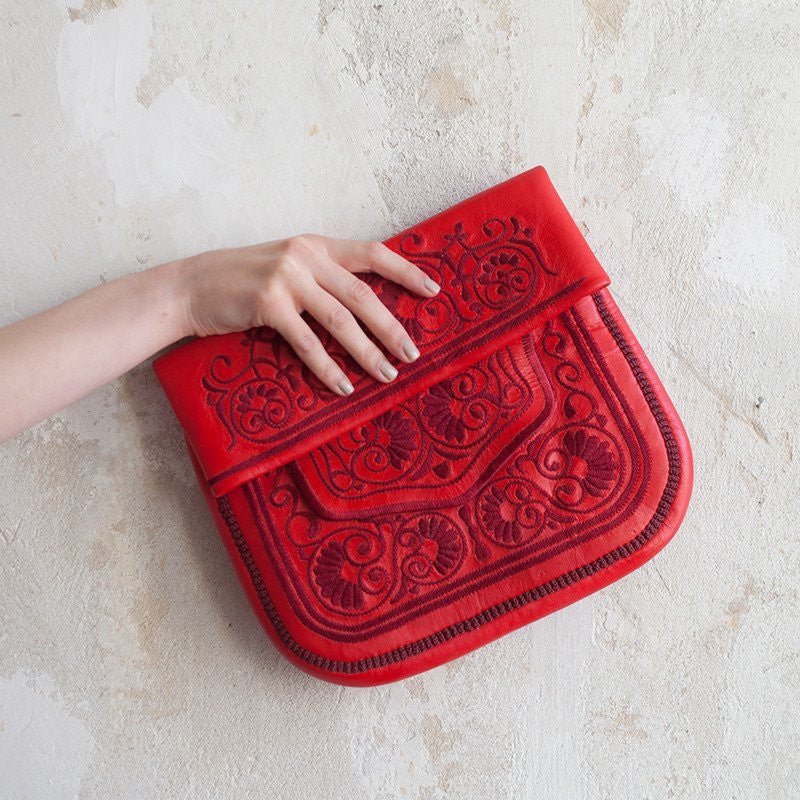 The Berber Bag in red, held against a pale wall