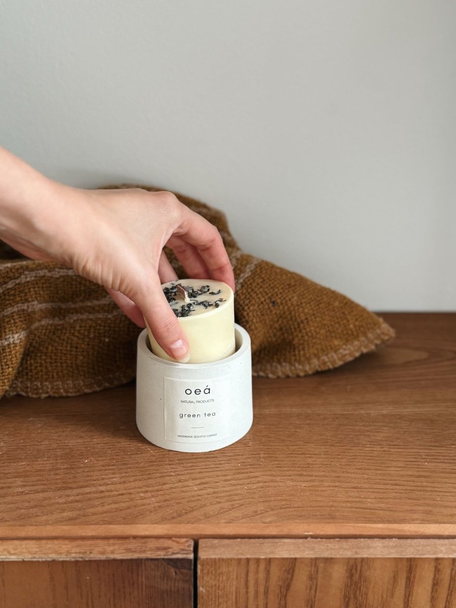 A refill going into its vessel, the wooden wick and the green tea leaves already set in the wax.