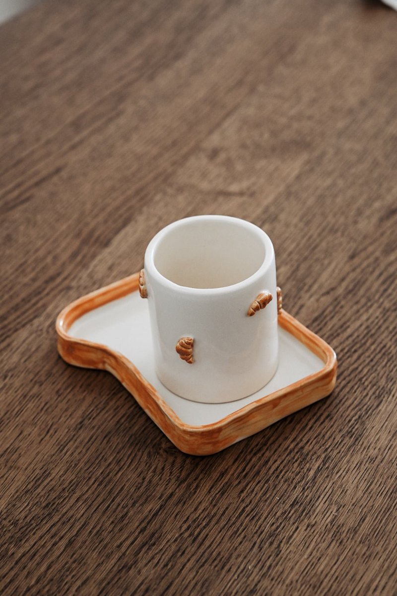 A toast-shaped plate with a croissant-decorated mug sitting on it
