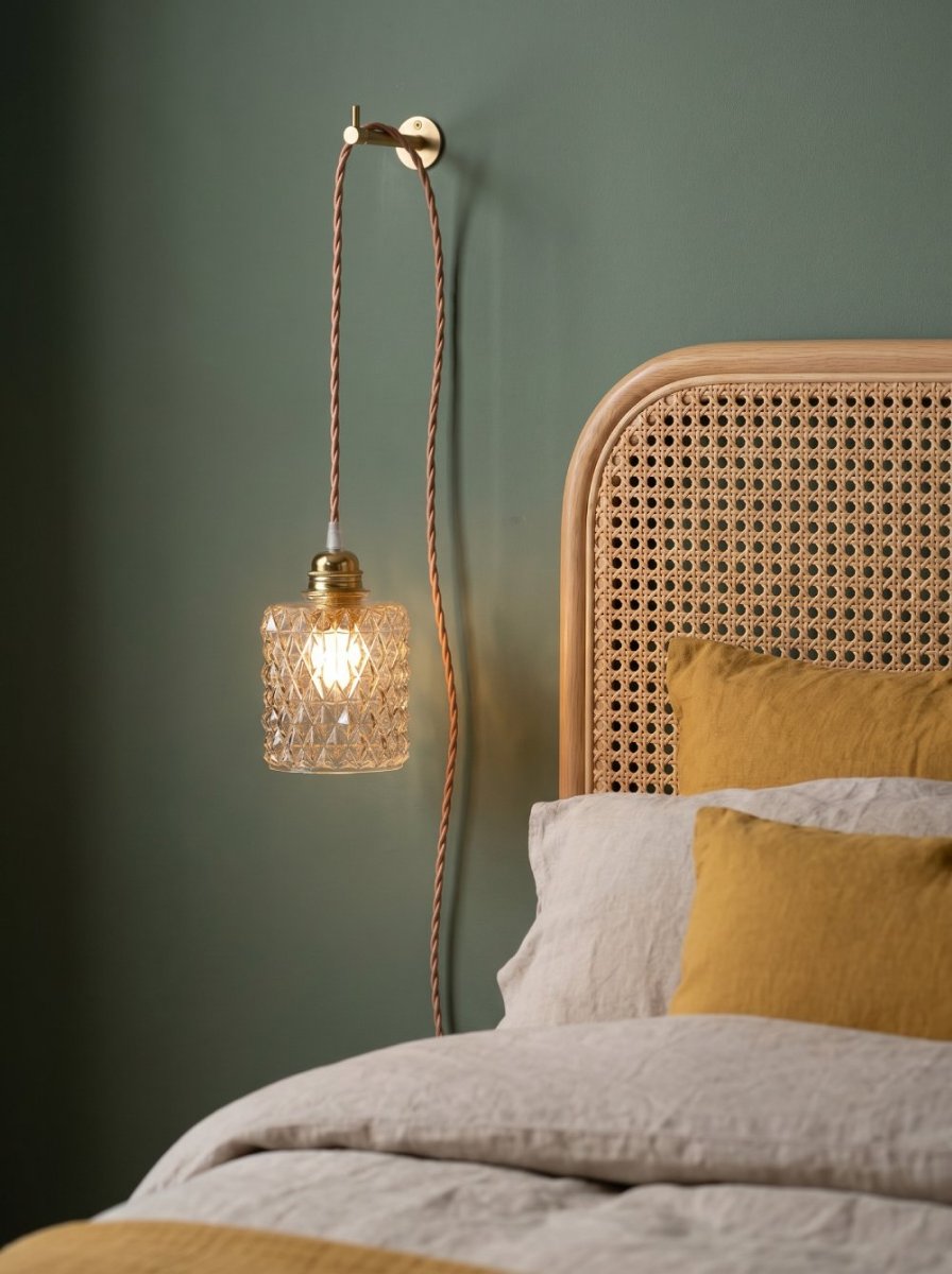 A hand lamp lit and hanging by its brass hook above a cane headboard.