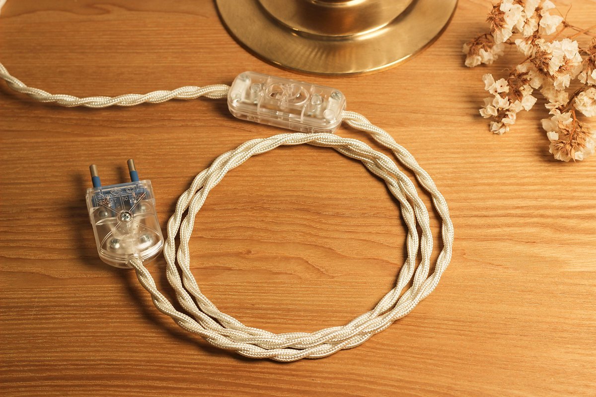 An ivory twisted cable coiled on oak, with a switch, a plug and a brass base plate.