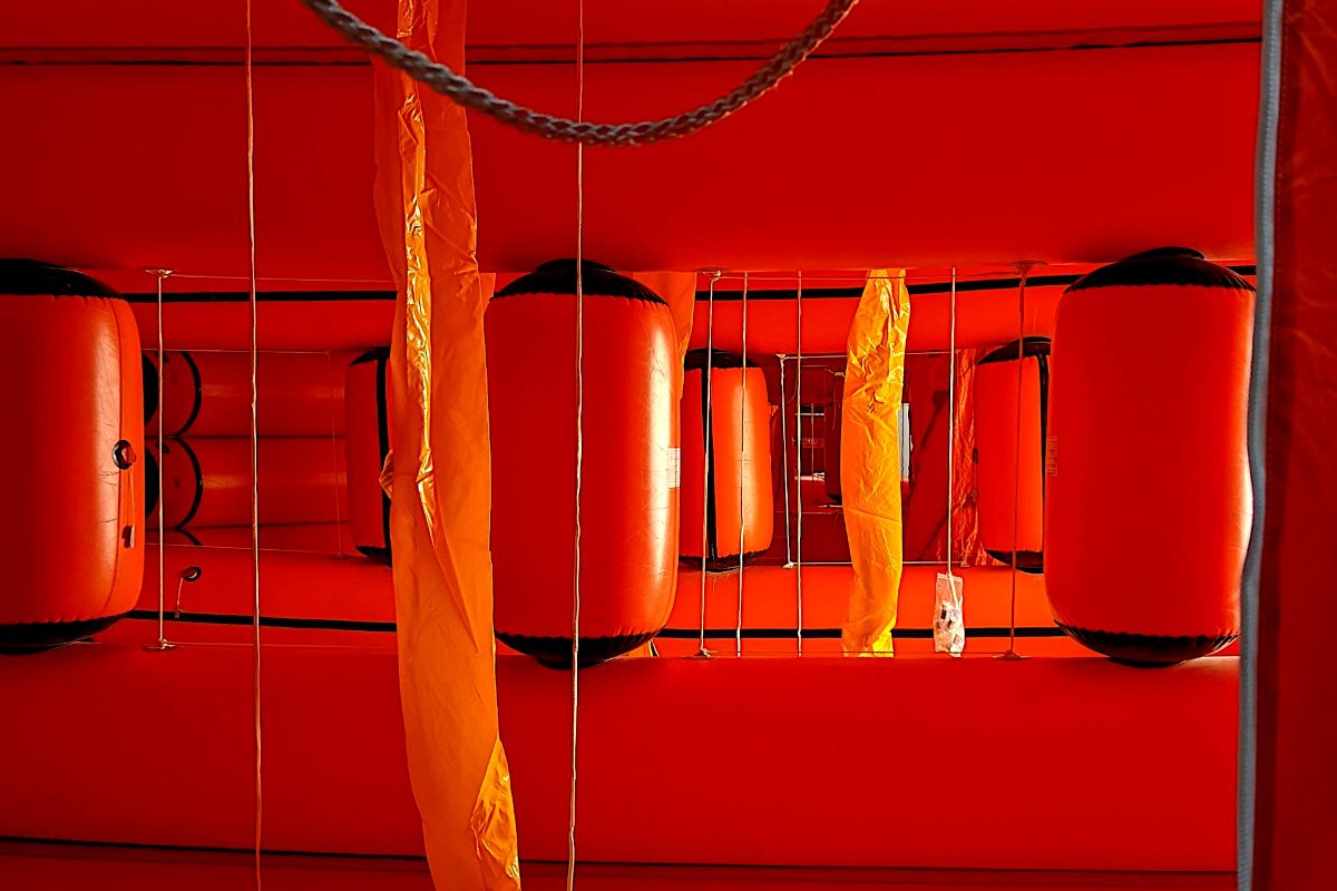 Inside an inflated life raft: the orange canopy, the tubes and hanging lines