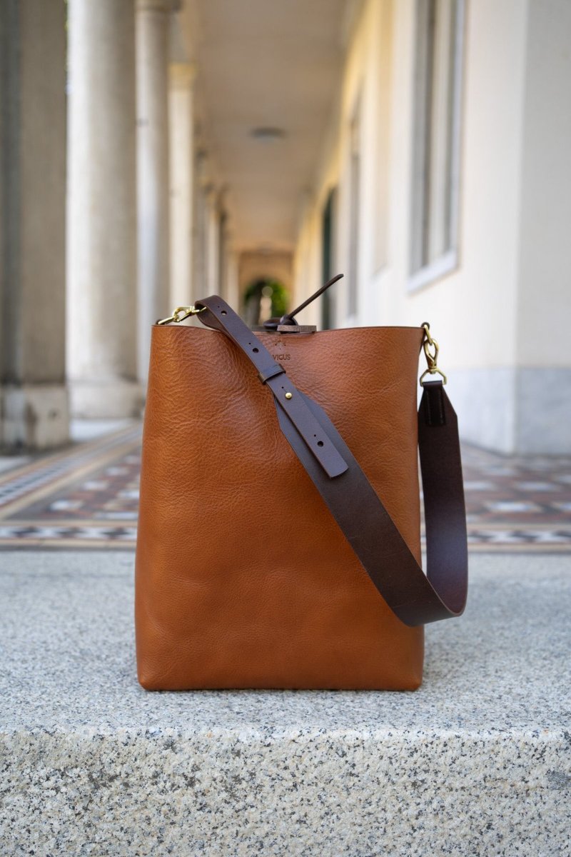 A tan leather tote on a stone plinth in an open arcade of round columns.