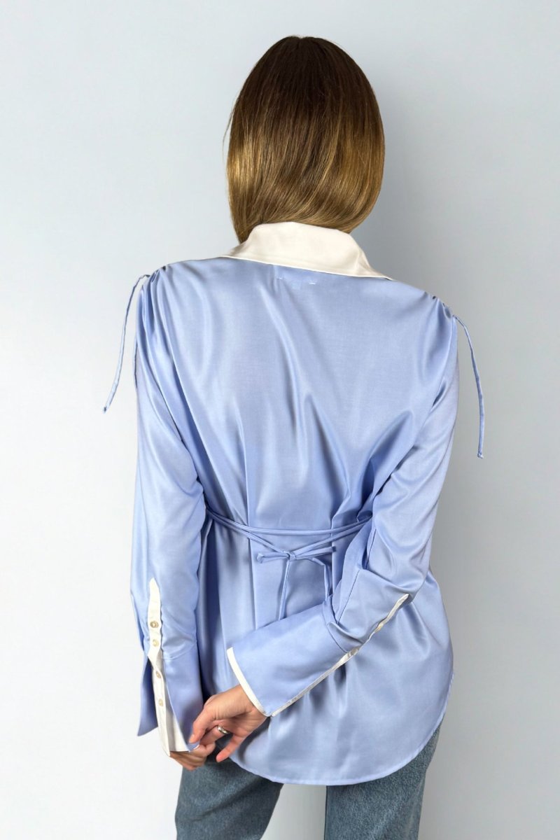 The blue shirt from the back, worn over jeans, ties gathered at both shoulders, the waist band knotted in a bow, cuffs and collar in white.