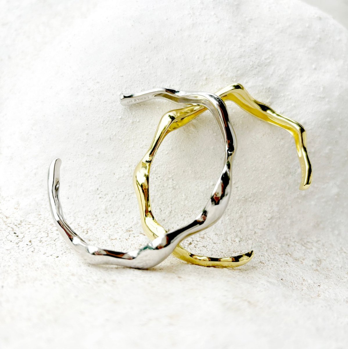 The silver and gold-vermeil Jasmine cuffs resting on pale stone.