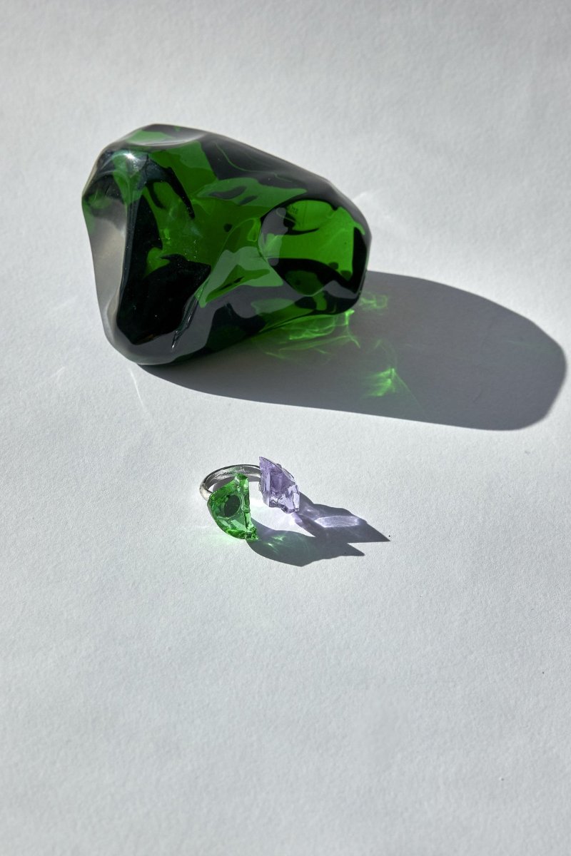 A green crystal block throwing a long shadow, a ring with green and violet splinters set in front