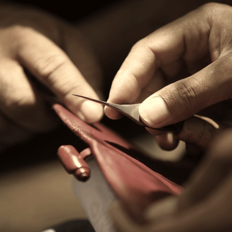 Hands trimming the edge of red leather with a fine blade