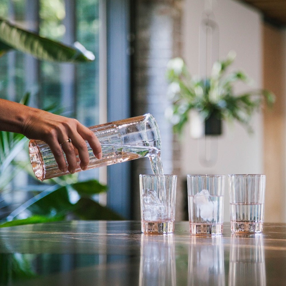 A hand tipping the fluted Reed carafe over three glasses of ice.