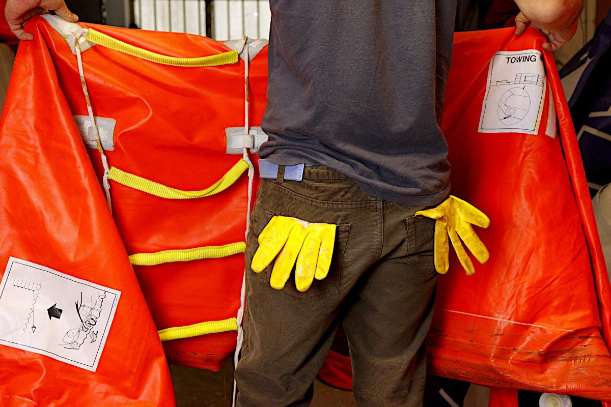 Someone holds open a length of orange raft fabric, the yellow straps still attached